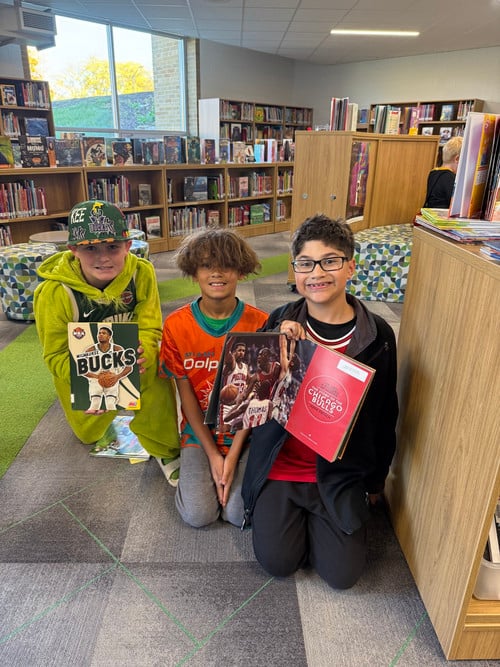 Students kneeling in the library holdling their favorite books for Book Character Day.